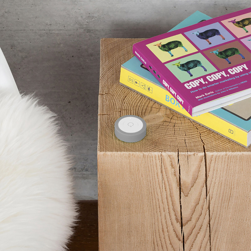 Grau-weißer, runder myStrom WiFi Button auf einem Nachttisch mit Büchern