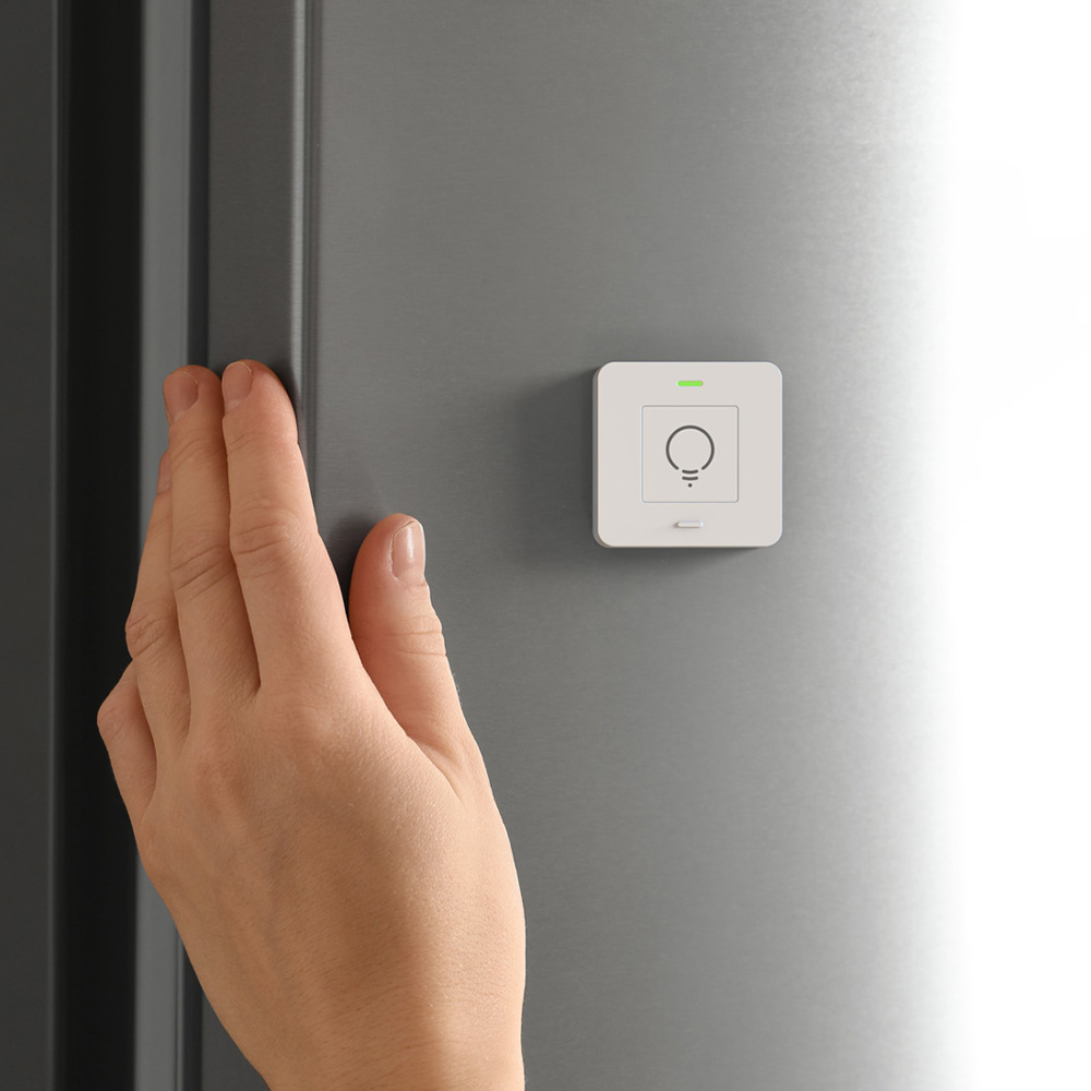 Weißer, quadratischer myStrom WiFi Button Plus an einer grauen Wand mit einer Hand daneben