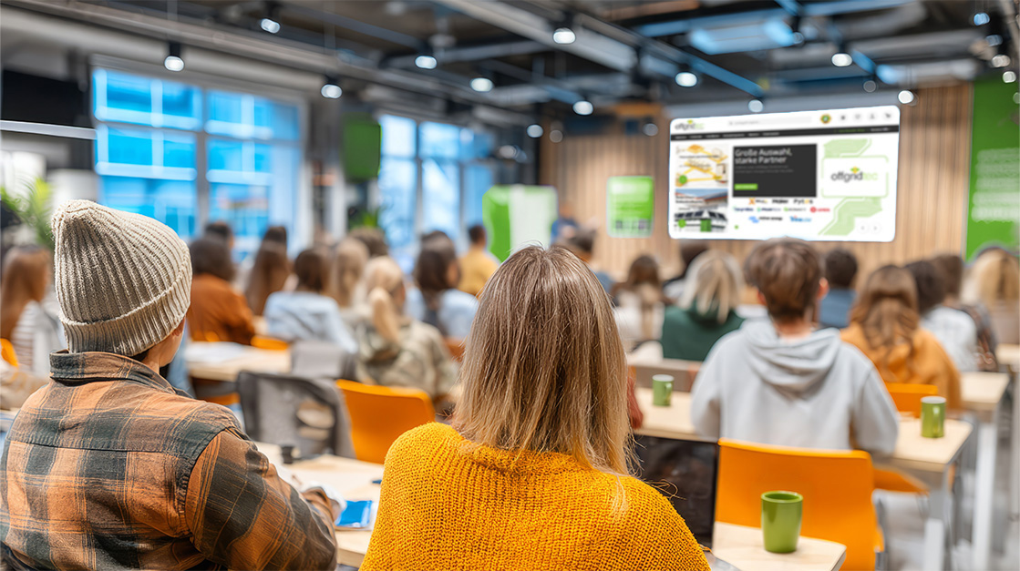 Ein Schulungsraum mit Menschen die alle in Richtung virteuller Tafel schauen mit der Offgridtec Website als Vorschau